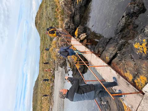       Travellers cross a narrow wooden bridge over tide pools and rocks on a coastal hike.
  