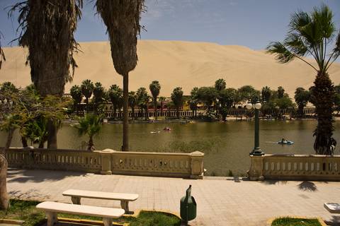       Desert oasis of Huacachina with palm-lined lagoon, sand dunes and kayakers enjoying the water.
  
