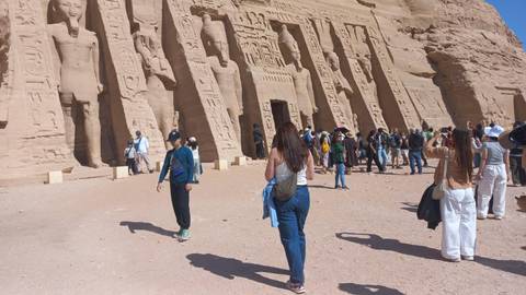       Tourists gather in front of the colossal carved façade of Abu Simbel temple in the desert.
  