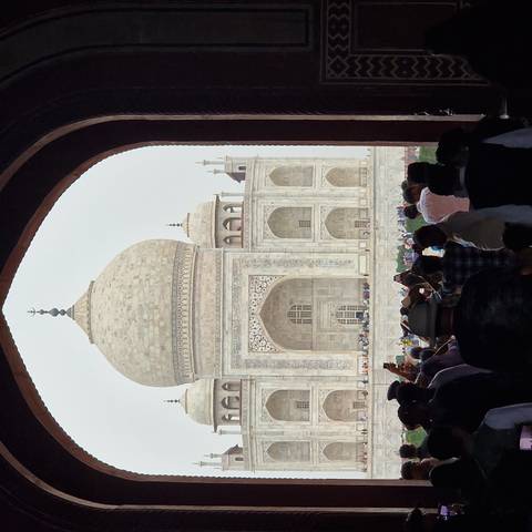       Crowd frames the Taj Mahal through a grand archway, emphasizing its symmetrical marble beauty.
  