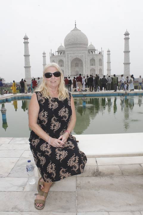       Woman sits near the iconic Taj Mahal reflecting pool with tourists and monument in background.
  