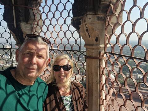       Couple taking a selfie beside an ornate lattice stone screen high above a sprawling cityscape.
  