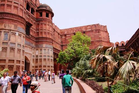       Interior courtyard of Agra Fort with tourists exploring ornate red-sandstone arches and greenery.
  