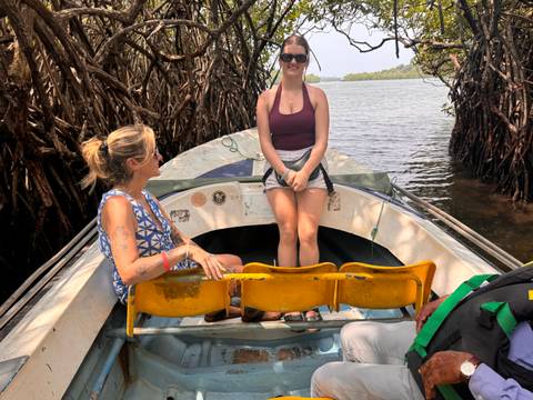       Two young women enjoy a small motorboat ride through mangrove-lined waterways.
  