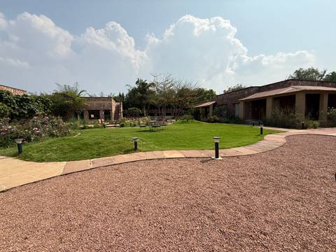       Eco-lodge complex with manicured lawn, stone paths, and cottage-style rooms under a partly cloudy sky.
  