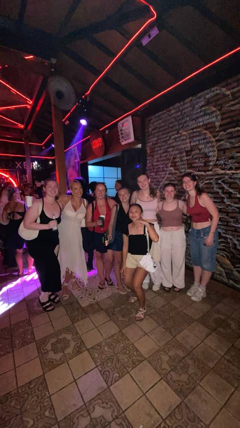       Friends pose together inside a dimly lit nightclub with neon lights and a busy crowd.
  