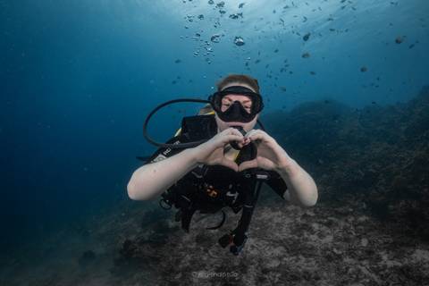       Scuba diver underwater forming a heart with hands amid clear blue water and coral seabed.
  