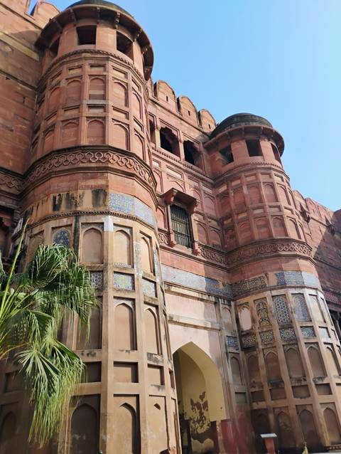       Red sandstone bastions and decorative tile inlay of Agra Fort rise against a clear sky.
  