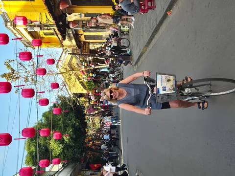       Smiling rider steers a bicycle through a bustling lantern-decorated street scene.
  