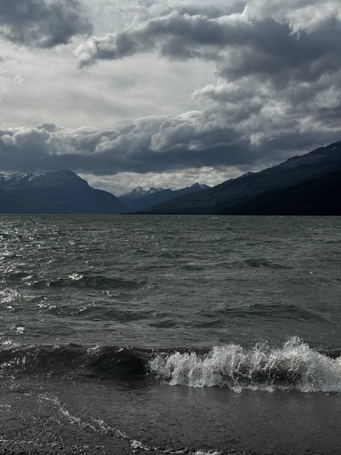       Wind-ruffled dark lake under brooding clouds with distant snowy peaks on the horizon.
  