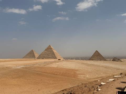       Iconic trio of Giza pyramids rising from the desert plain under hazy skies.
  
