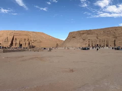       Twin rock-cut temples of Abu Simbel fronted by colossal statues, visited by many tourists in an open desert setting.
  