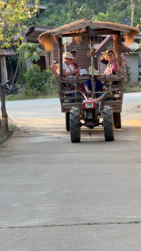       Small red farm tractor pulling a wooden cart along a rural paved road.
  