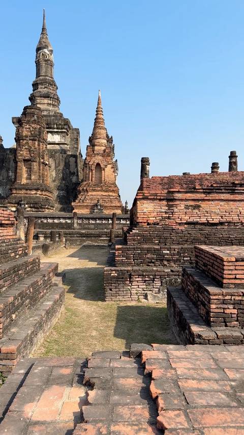       Ancient brick ruins and Buddha statues of Sukhothai Historical Park under clear skies.
  
