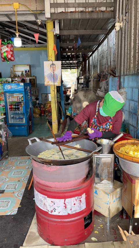       Street vendor frying banana chips in a giant wok using wooden paddles at a local Thai market.
  