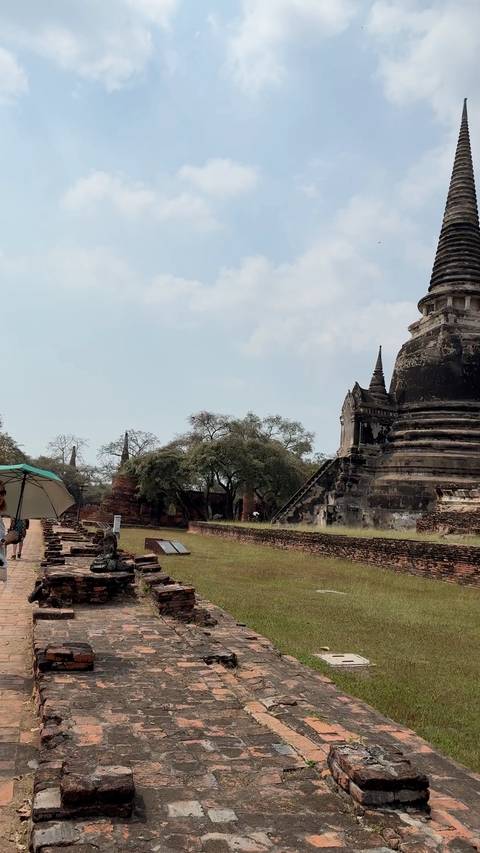       Ancient stupa and brick ruins at Ayutthaya Historical Park with a visitor holding an umbrella.
  