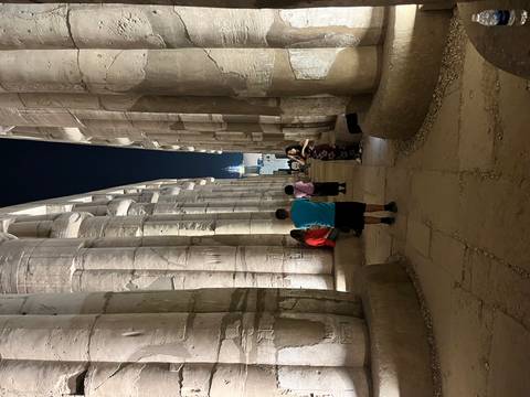       Visitors wander between towering illuminated columns inside Luxor Temple at night.
  