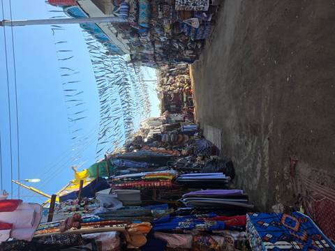       A quiet market lane lined with fabric stalls and overhead strings of bunting during daylight.
  