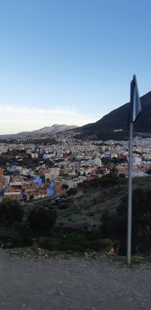       A sprawling hillside city with clusters of blue and white buildings surrounded by mountains.
  