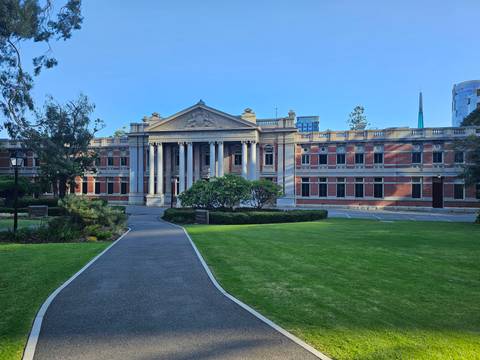       Elegant historic courthouse framed by lawns, pathway and trees under clear sky.
  