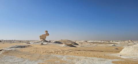       Isolated limestone pillar stands in vast flat desert beneath clear blue sky
  