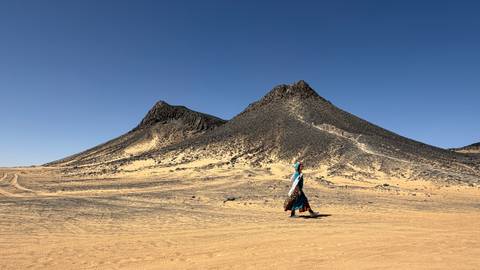      Traveller passes dark volcanic cones rising from golden desert sands
  