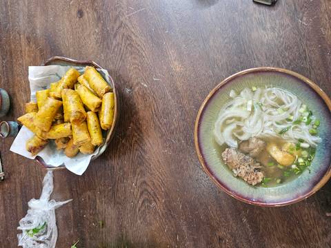      Overhead view of steaming beef noodle soup and golden fried spring rolls on wooden table
  