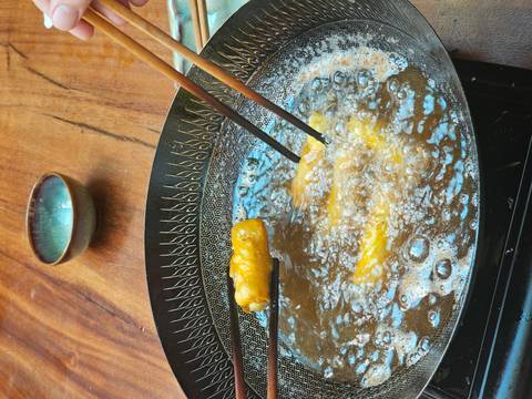       Spring rolls sizzling in oil inside patterned pan with chopsticks turning food
  