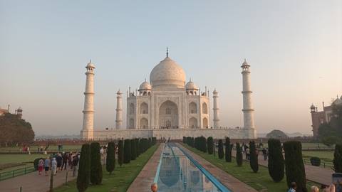       Symmetrical view of Taj Mahal with gardens and crowd in soft morning light
  