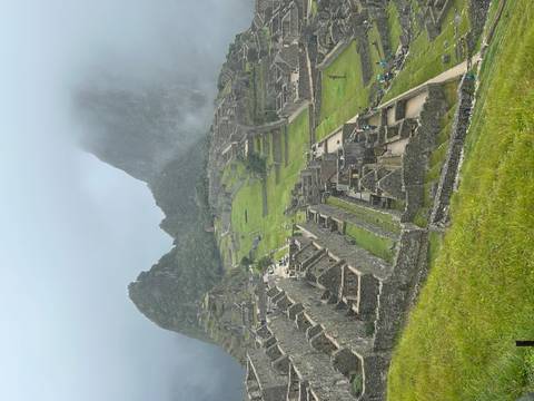       Machu Picchu’s stone terraces and temples emerge from lush green slopes under drifting mist and towering peaks.
  