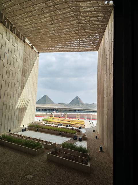       Framed view between modern museum walls reveals two pyramids rising against a cloudy sky.
  