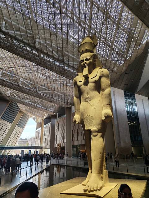       Massive sandstone pharaoh statue stands beneath a dramatic steel-and-glass roof of the museum atrium.
  