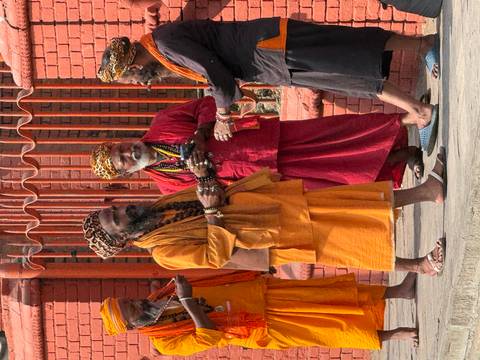      Group of colourfully dressed sadhus chat outside a red-brick shrine, draped in orange and crimson robes.
  