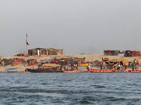       Makeshift riverbank camp with colourful boats and tents lining the sandy shore.
  