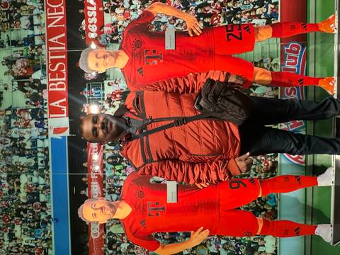       Visitor stands with Bayern Munich cut-outs in a football museum display.
  