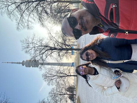       Winter family selfie with Munich’s Olympic Tower rising behind frosted trees.
  