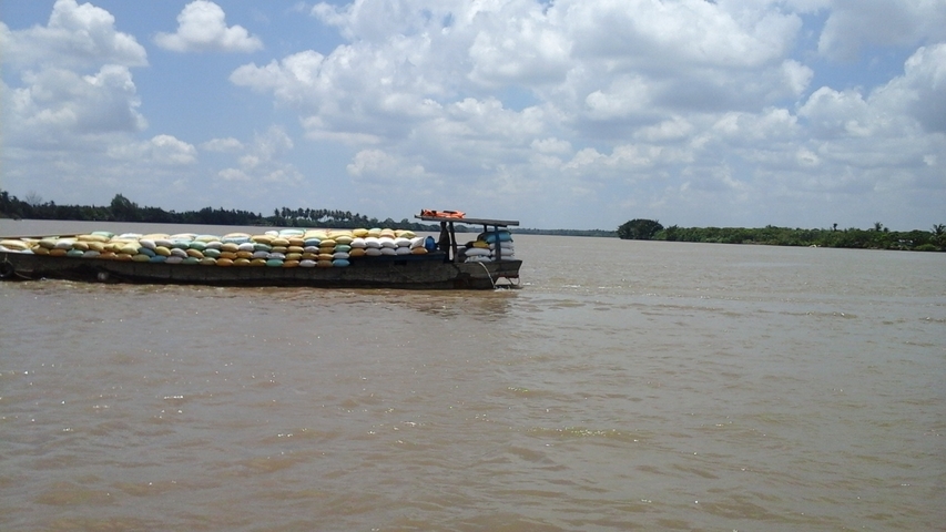       A boat laden with goods on a wide river under a cloudy sky.
  