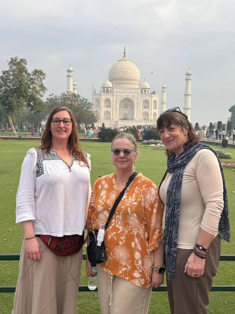       Group portrait with the Taj Mahal rising majestically in the background across its gardens.
  