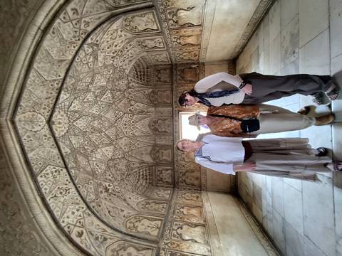       Three travellers stand inside an intricately carved marble chamber of a Mughal palace.
  