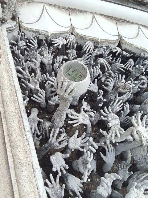       Concrete chalice held by dozens of gray sculpted hands, coins and banknote visible inside.
  