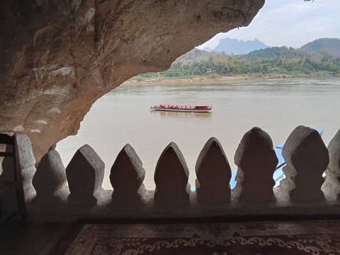       View from within a limestone cave looking out over the Mekong River where a longboat drifts past.
  