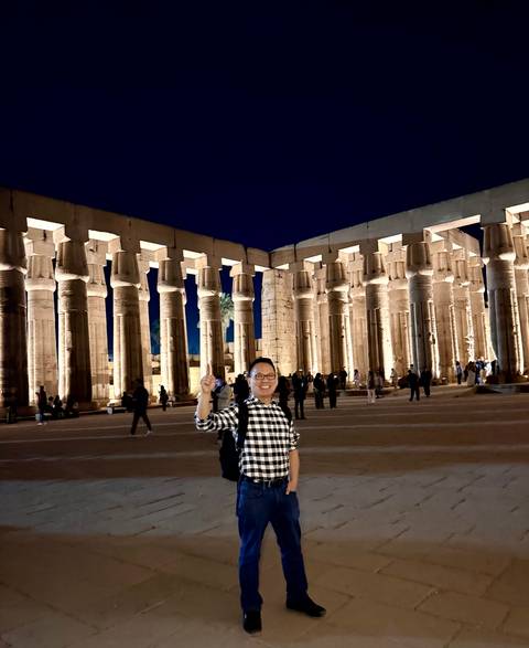       Visitor stands in front of illuminated columns of Luxor Temple at night.
  