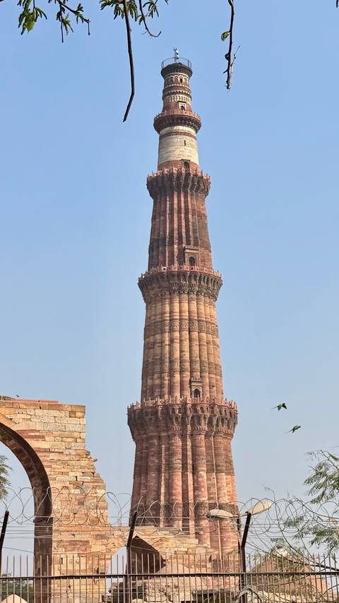       Tall sandstone Qutub Minar tower rising against a clear blue sky
  