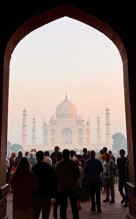       Hazy sunrise view of the Taj Mahal framed by a dark archway
  
