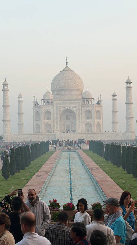       Front view of the Taj Mahal with reflecting pool and crowds of visitors in morning haze
  