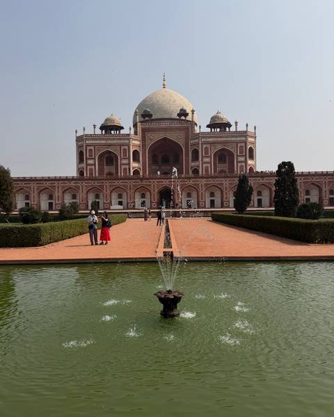       Humayun’s Tomb with garden fountain and visitors strolling along the sandstone pathway
  