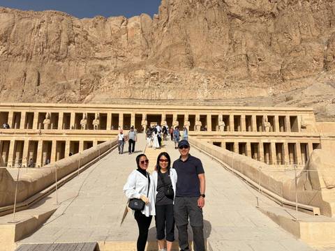       Visitors pose on the ramp leading to the colonnaded facade of the Mortuary Temple of Hatshepsut set against rugged desert cliffs.
  