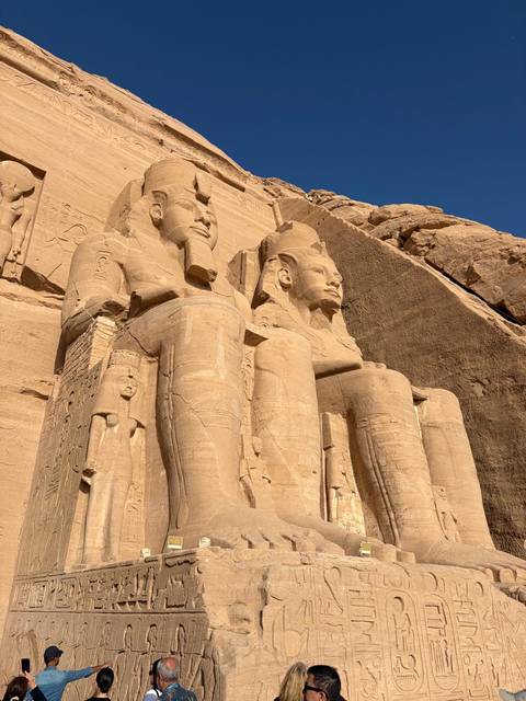       Close-up view of the colossal seated statues carved into the sandstone facade of Abu Simbel temple bathed in bright sunlight.
  