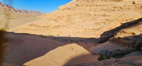       Shadow of a large rock bridge falls across a sandy valley and sandstone cliffs.
  