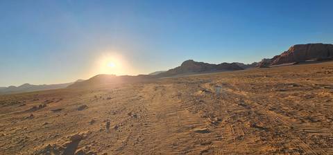       Low sun touches the horizon over a vast sandy desert plain creating long shadows and golden light.
  